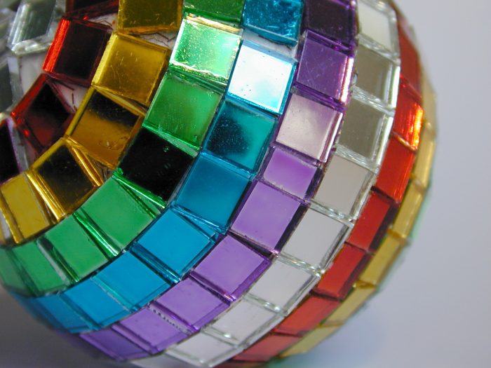 Unusual vibrant multicolored festive bauble with rows of tiny mosaics in the colours of the rainbow, close up view for a colorful Christmas or holiday background